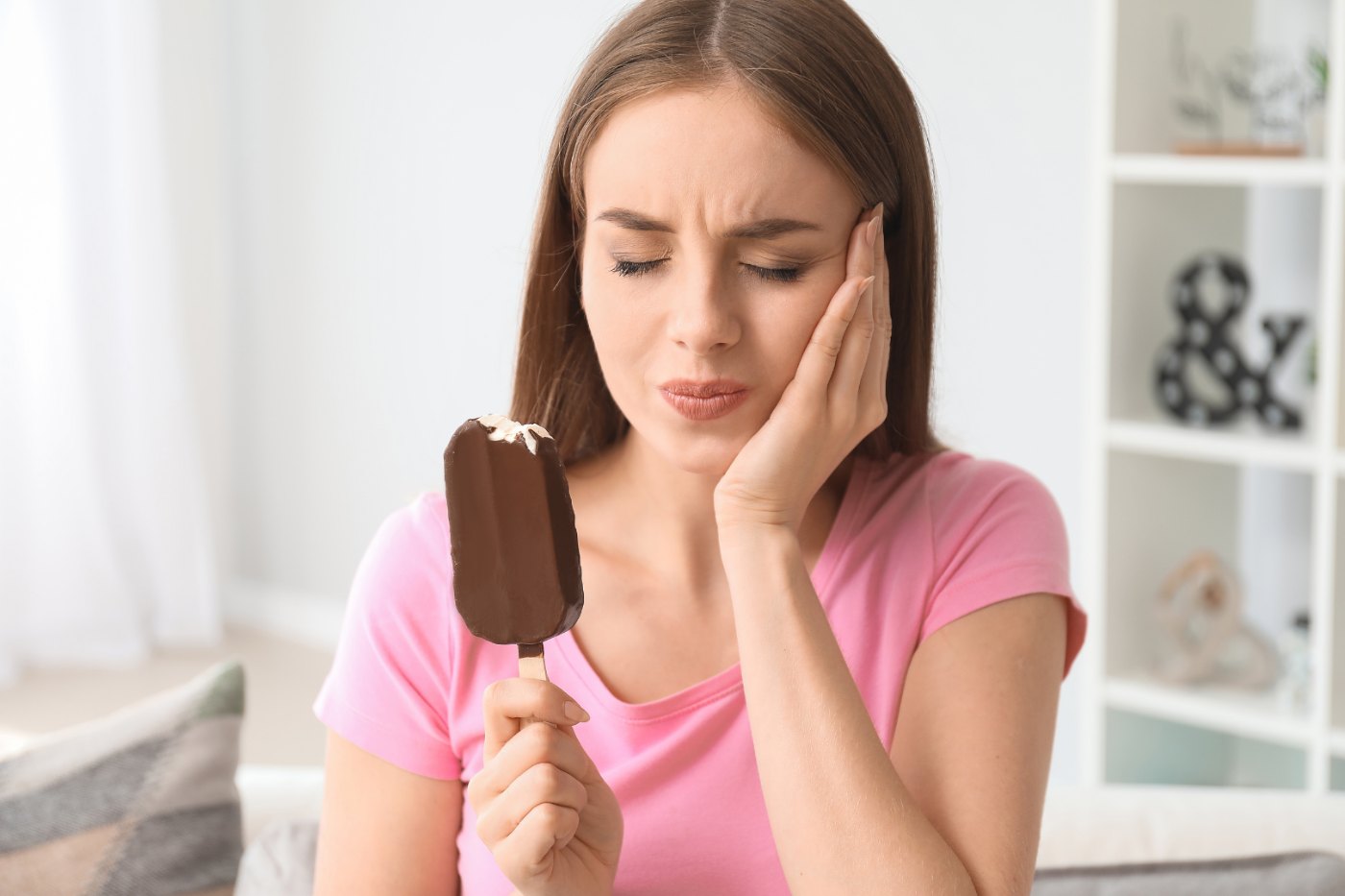 Mulher sentindo sensibilidade dentária ao comer sorvete